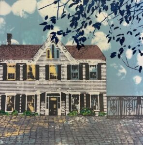 An artwork by Jean Burdick using silkscreen on vellum. A house is featured in front of a cobbled sidewalk with an iron decorative fence on the right. A cloudy looking sky is in the background with a few branches and leaves barely touching the roof of the house in the foreground. The windows of the house are surrounded by shutters.