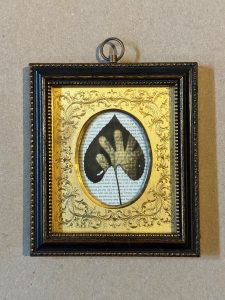 Framed picture. Oval in the center with a leaf and what appears to be a hand within it.